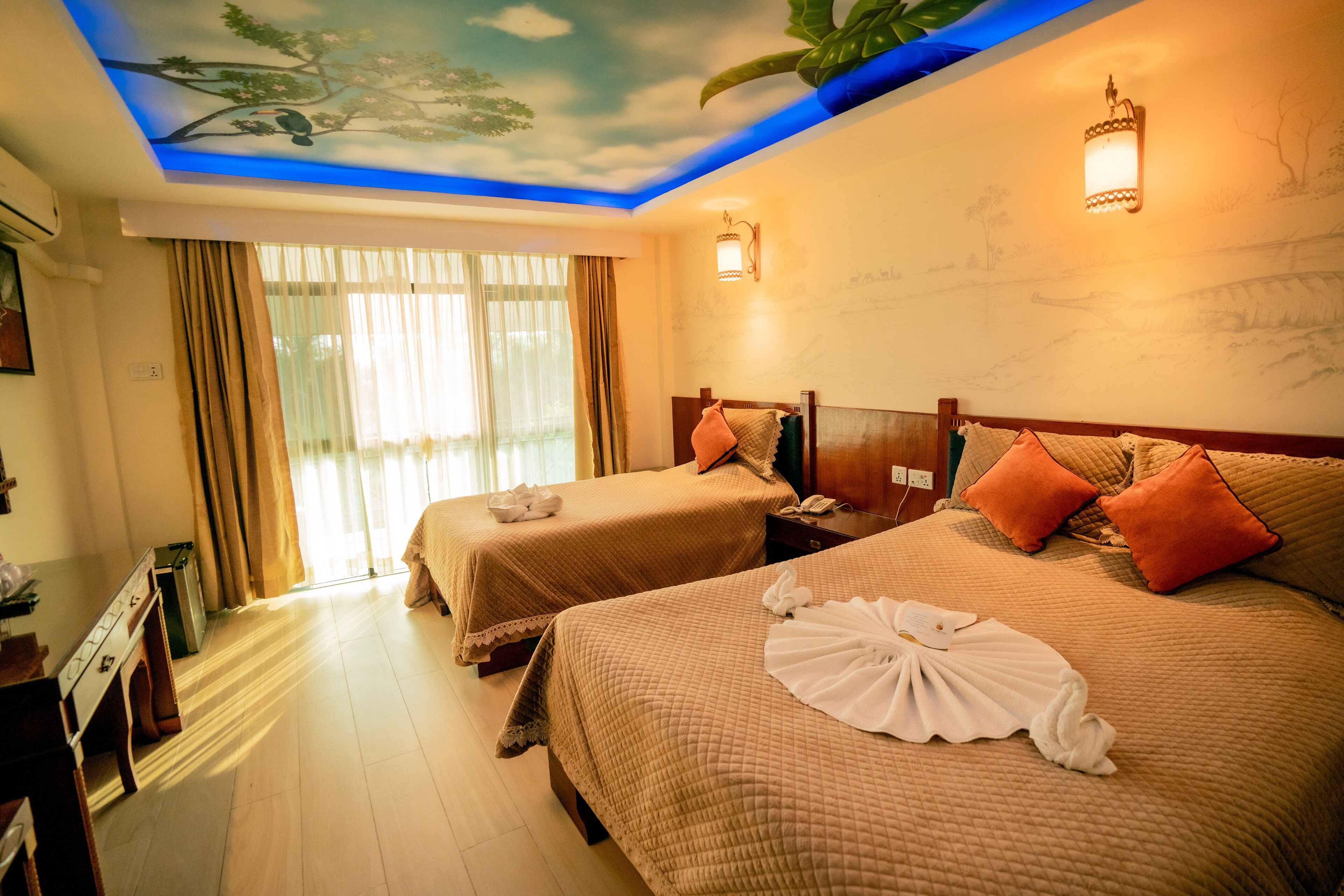 Een hotelkamer met twee bedden, een bureau en een muurschildering aan het plafond.