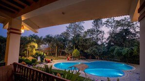 Piscina com deck de madeira e espreguiçadeiras, rodeada por vegetação exuberante e árvores.
