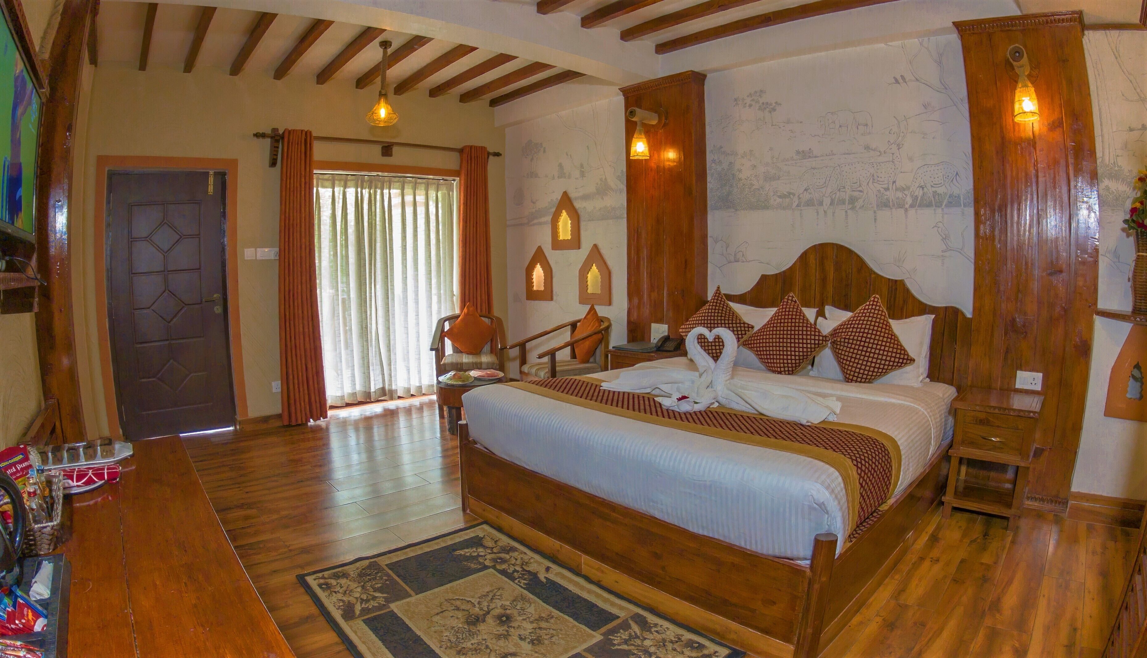 A hotel room with a wooden bed, a large window with curtains, a wooden floor, and a wall with a mural.