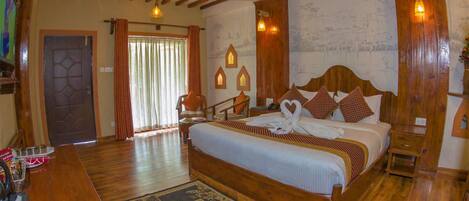 A hotel room with a wooden bed, a large window with curtains, a wooden floor, and a wall with a mural.