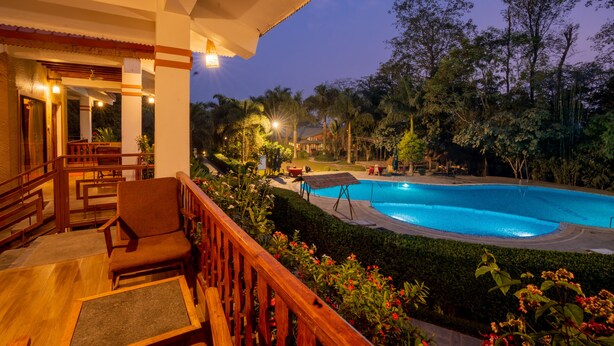 Área da piscina com deck de madeira, assentos e vista para o verde ao redor.