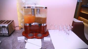 A juice dispenser with two labeled containers, a toaster, and shot glasses lined up on a marble countertop.