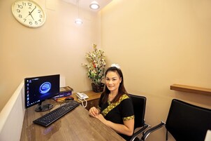 A woman sitting at a desk with a computer, a clock, and a plant.