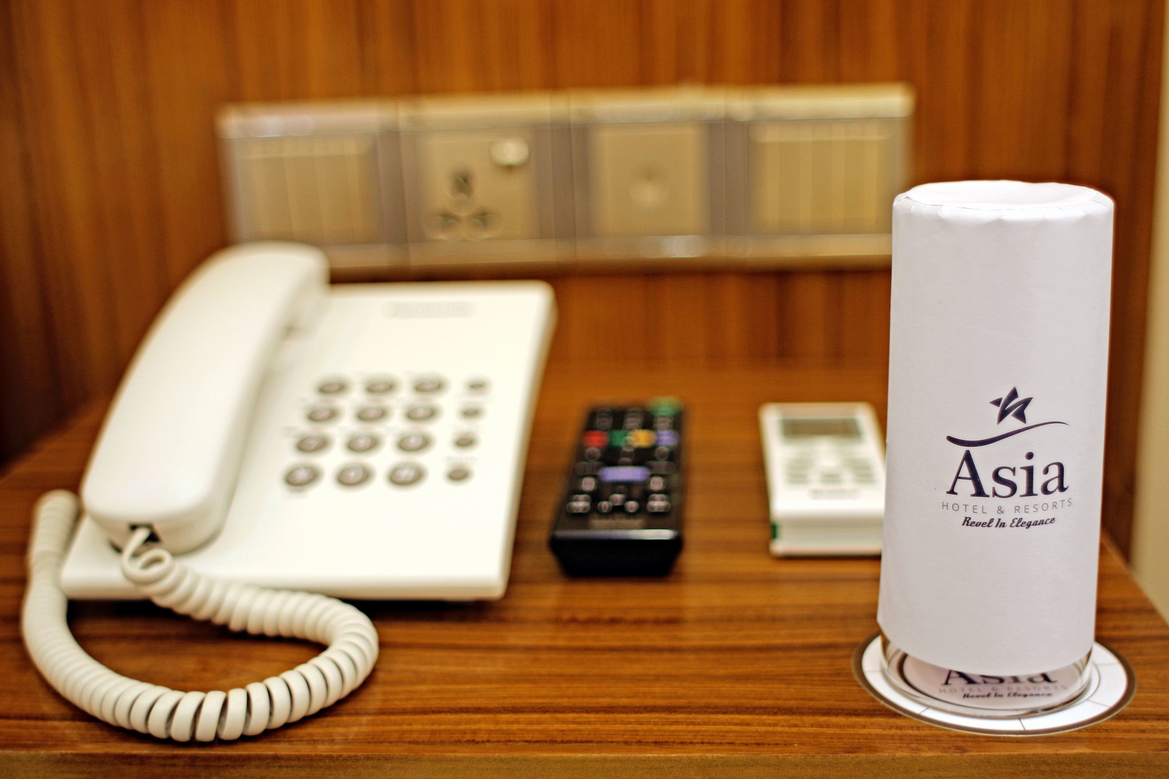 Una reception di hotel con un telefono bianco, un telecomando e un depliant arrotolato di Asia Hotel & Resorts.