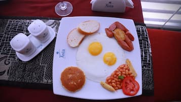 Een ontbijtbord met eieren, worstjes, toast, bonen en tomaat op een tafel met een rode tafelkleed.