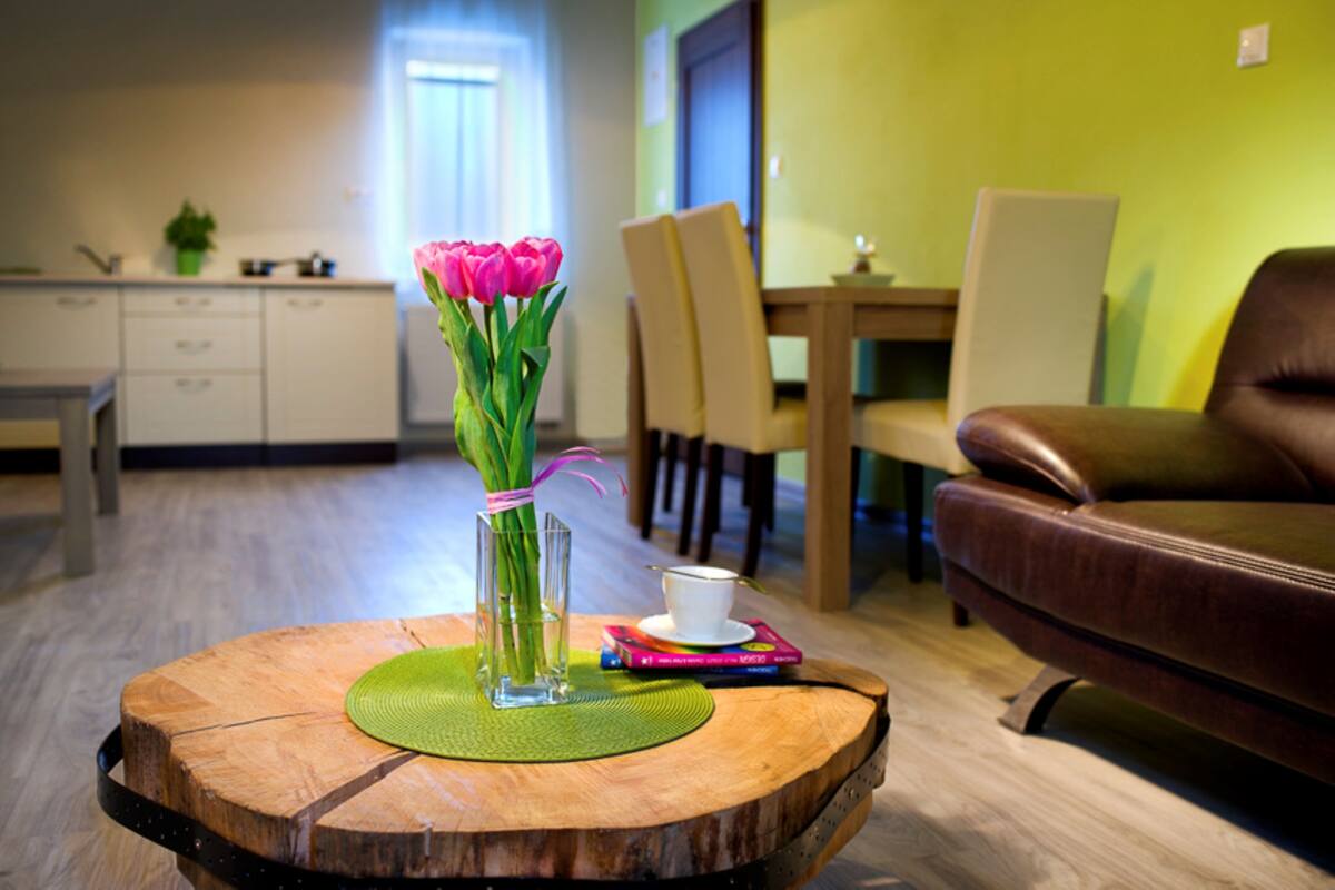 A wooden coffee table with a vase of pink tulips, a white cup, and a book.