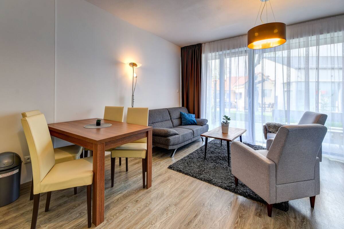 A modern living room with a wooden dining table, a grey sofa, and a grey armchair.