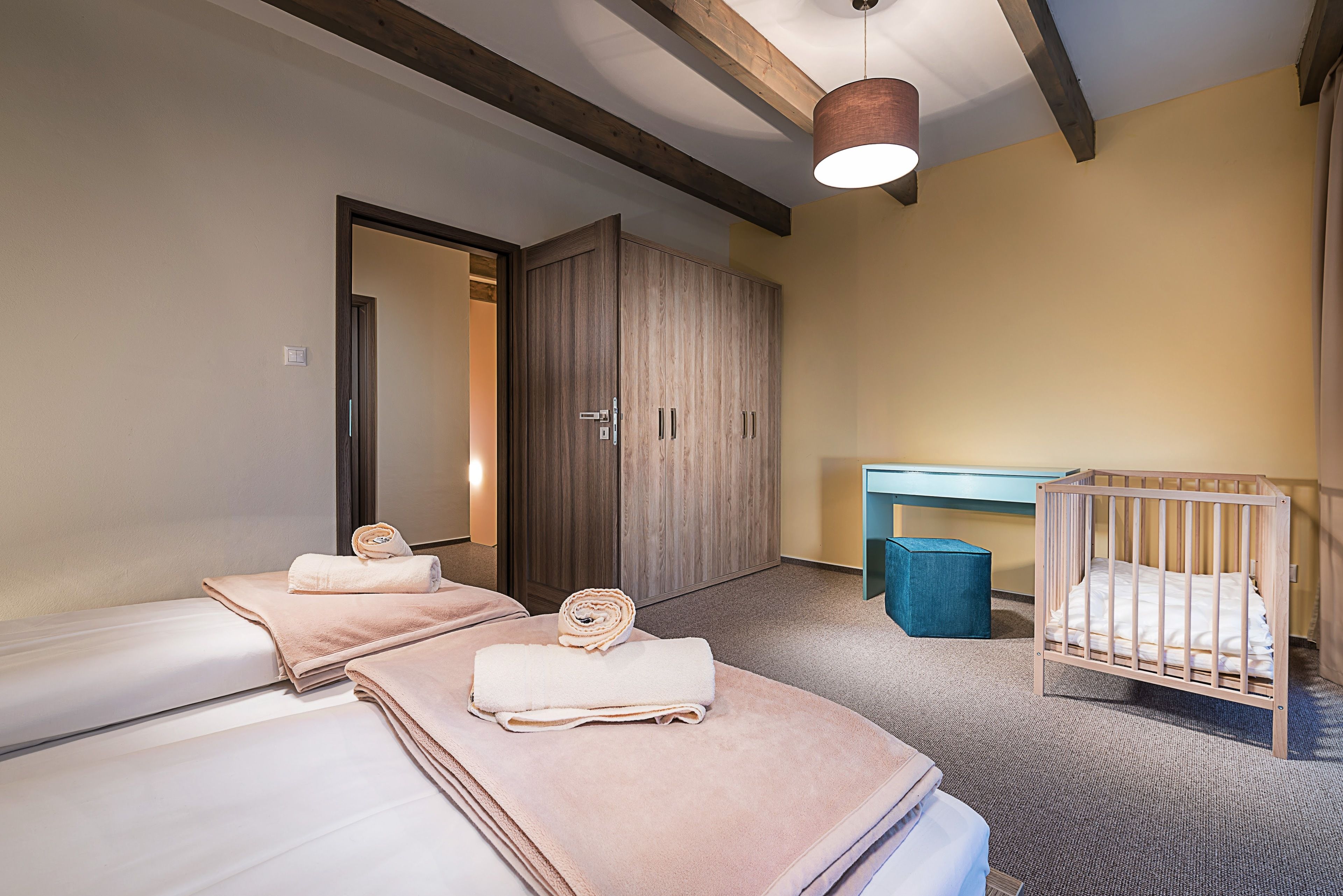 Habitación de hotel con dos camas, un armario de madera, un escritorio, una cuna y una lámpara colgante.