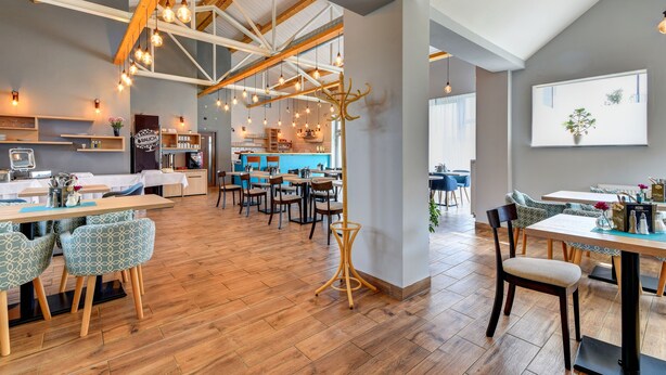 A spacious dining area with wooden flooring, multiple tables, and chairs. There are hanging light fixtures and a large window providing natural light. - Apartments Ceresnovy Sad (Mengusovce)