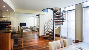 Un salon moderne doté d’un escalier à volutes, de parquet et d’un coin repas avec une table en verre.