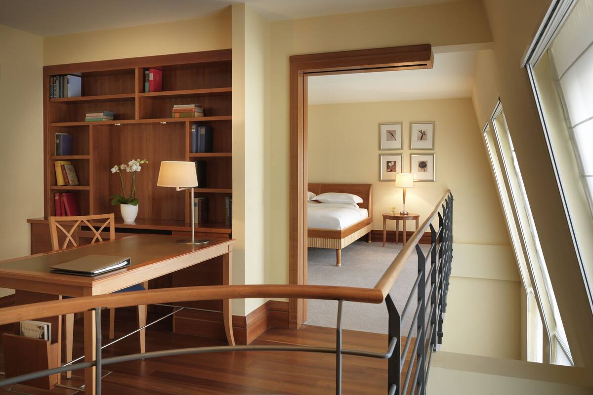 Ein Hotelzimmer mit Holztisch, Bücherregal und einem Bett mit Nachtschränkchen.