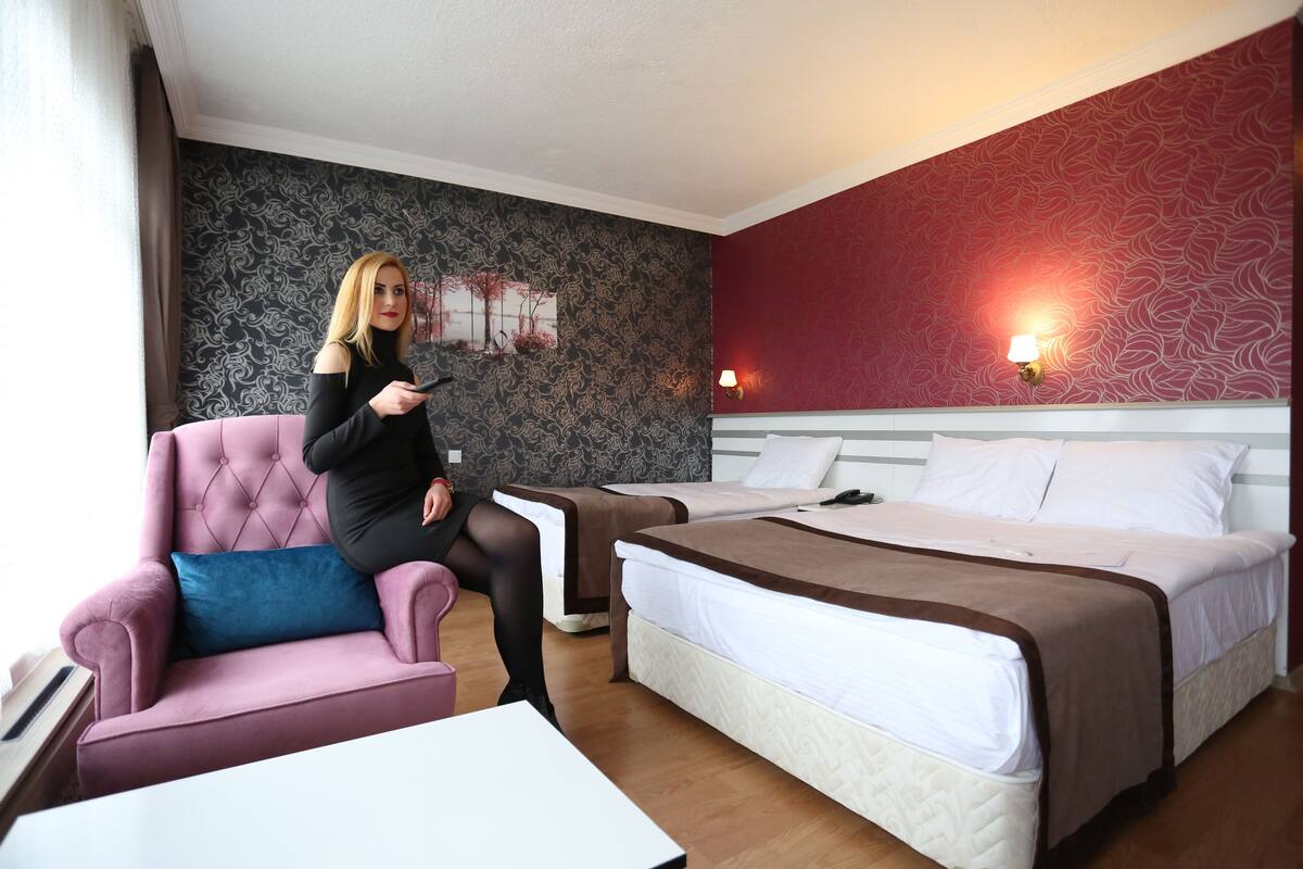 A hotel room with a pink armchair, two beds, a nightstand, and a wall with a decorative panel.