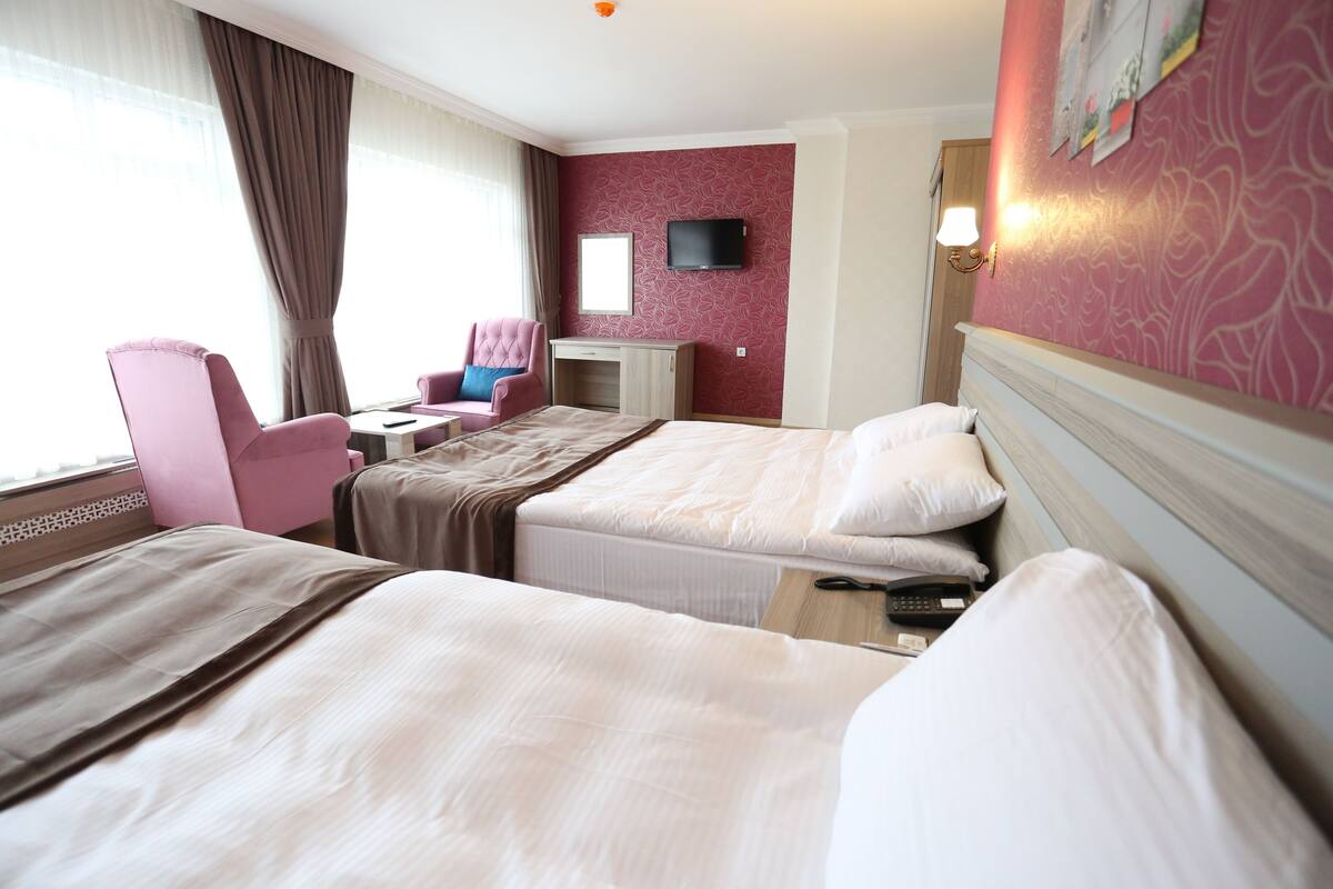 A hotel room with two beds, a desk, a chair, a TV, and a window with curtains.
