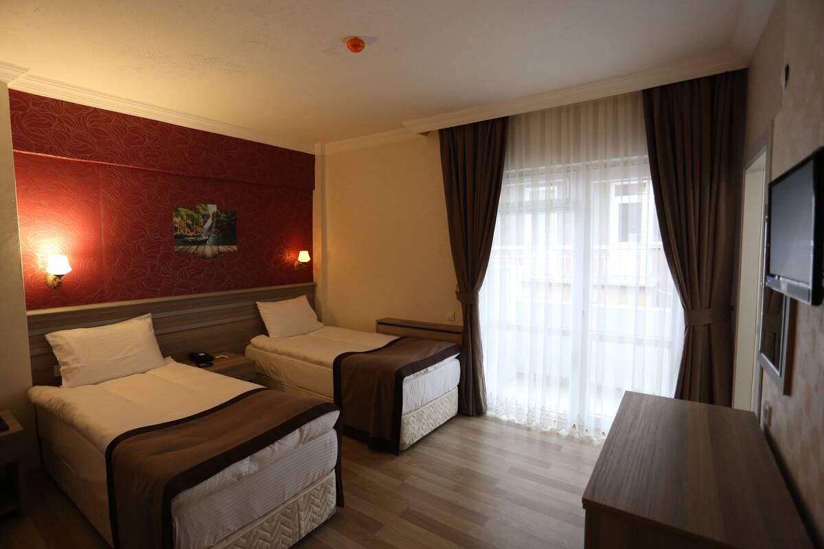 A hotel room with two beds, a TV, a desk, and a window with curtains.