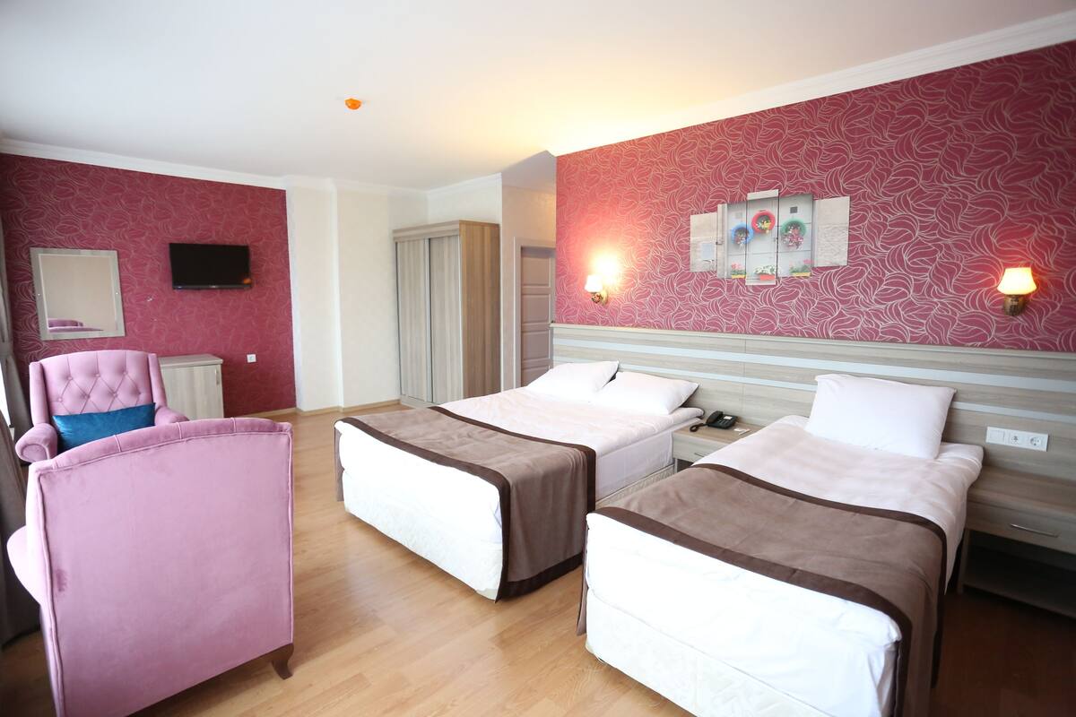 A hotel room with two beds, a pink armchair, a television, and a wall with decorative lights.