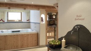 A modern bathroom with a wooden bathtub, a stone sink, and a bowl of fruits. - Hotel Augarten (Neustift Im Stubaital)