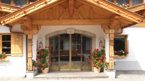 A wooden building with a large entrance, potted plants, and a sign above the door. - Hotel Augarten (Neustift Im Stubaital)