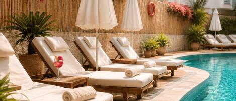 A poolside area with lounge chairs, umbrellas, and potted plants.
