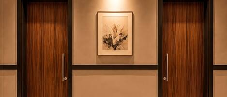 A hallway with two wooden doors, a framed artwork, and a marble floor.