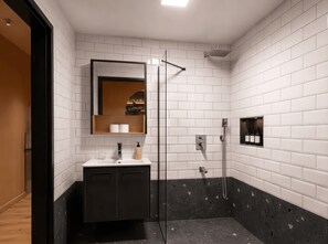 A modern bathroom with white subway tiles, a glass shower enclosure, a wooden vanity, and a black marble accent wall.