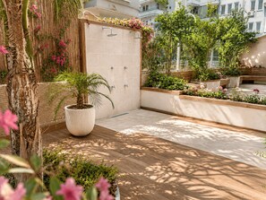 A rooftop garden with a large potted palm tree, a wooden deck, and a wall with a built-in shower.