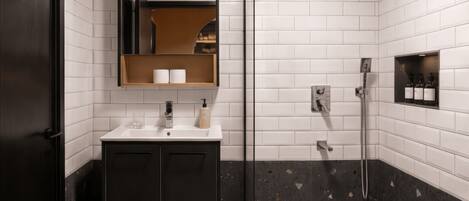 A modern bathroom with a glass shower enclosure, a dark-toned vanity, and a white tiled wall.