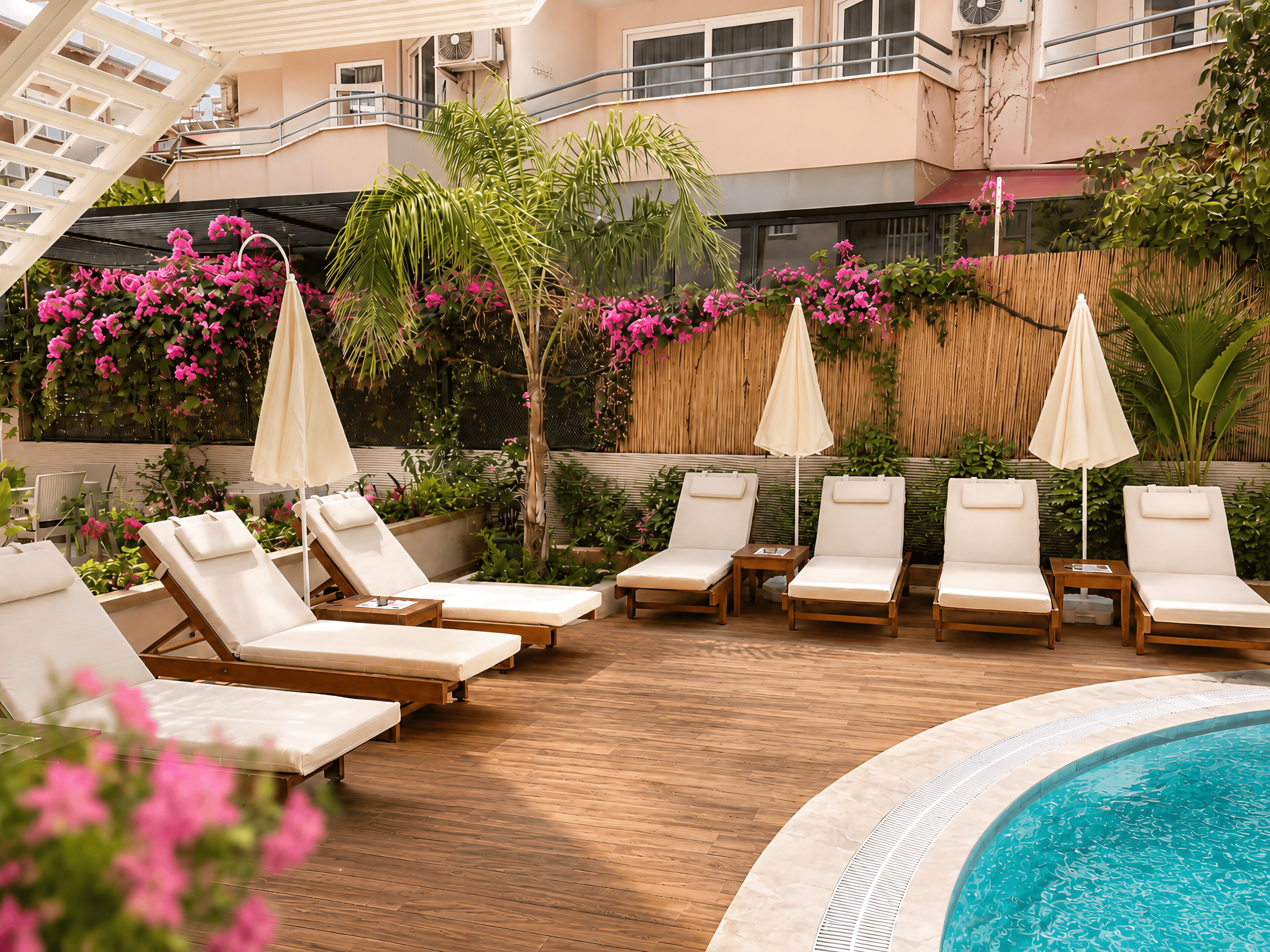 A poolside area with lounge chairs and umbrellas, surrounded by lush greenery and pink flowers.