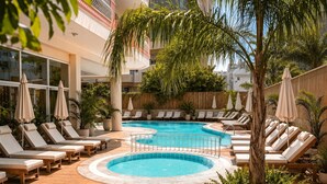 A pool area with lounge chairs and umbrellas, surrounded by greenery and a building facade. - Bella Rose Apart Hotel (Alanya)
