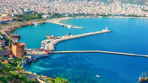 A coastal cityscape with a prominent lighthouse, a historic tower, and a marina with boats. - Bella Rose Apart Hotel (Alanya)