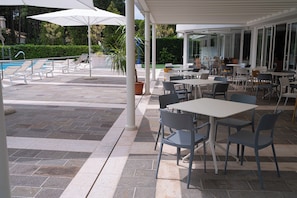 Une terrasse extérieure avec des tables et des chaises, une piscine et des parasols.