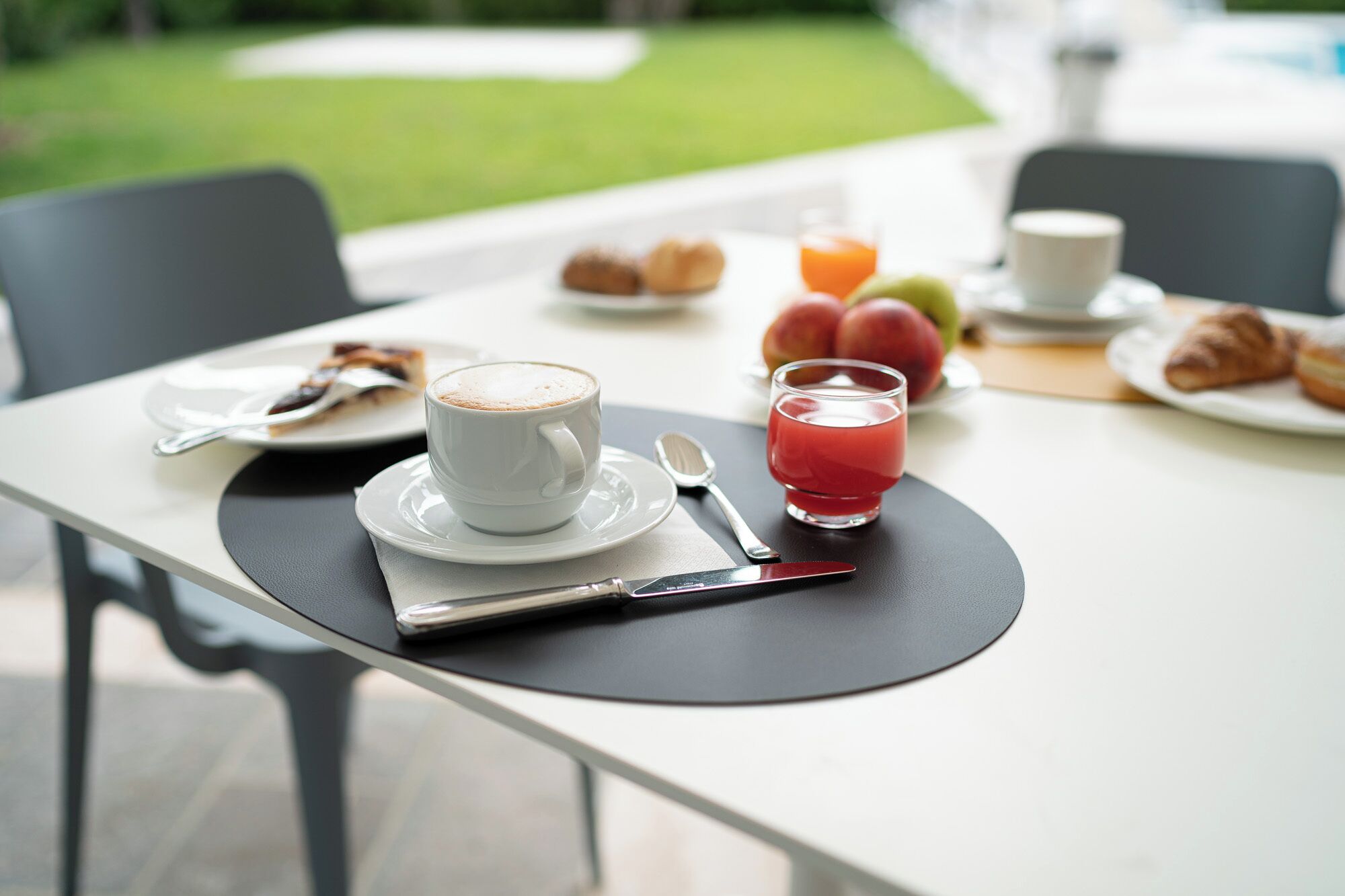 Ein Frühstückstisch mit einer Tasse Kaffee, einem Glas Saft, Croissants und Obst.