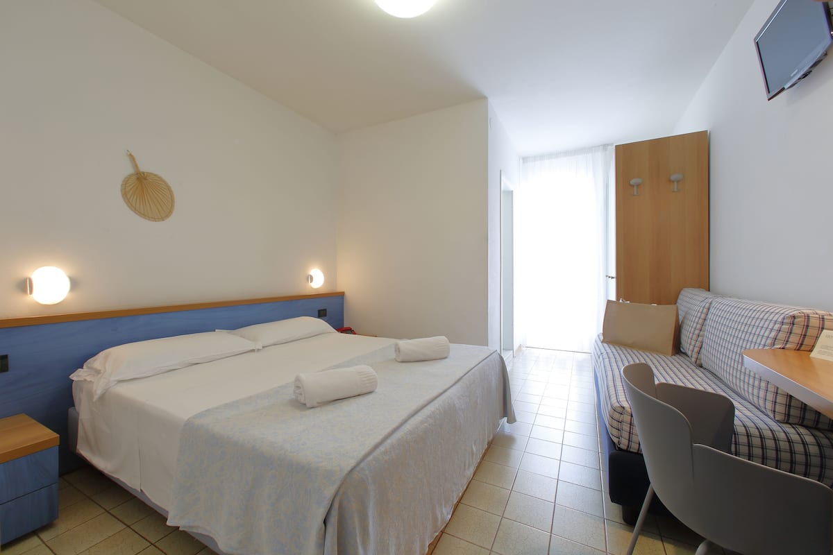 Una habitación de hotel con una cama, un escritorio, una silla y un televisor en la pared.