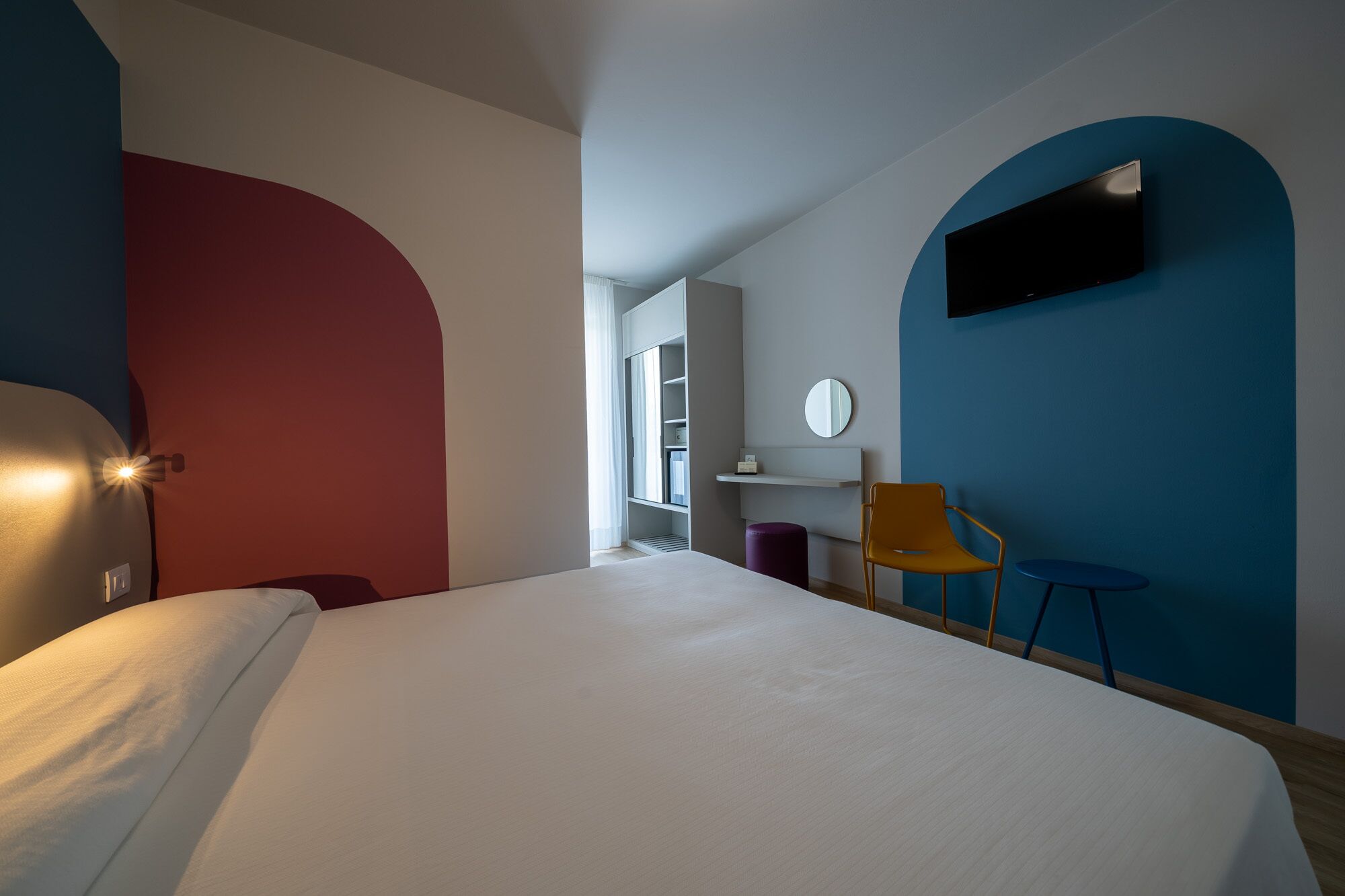 Een moderne hotelkamer met een groot bed, een bureau met stoel, een aan de muur bevestigde televisie en een kledingkast.