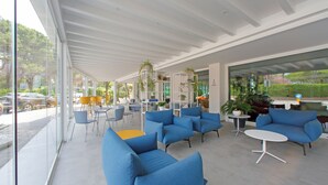 A modern outdoor seating area with blue sofas and chairs, a white table, and potted plants. - Hotel Smeraldo (Lignano Sabbiadoro)