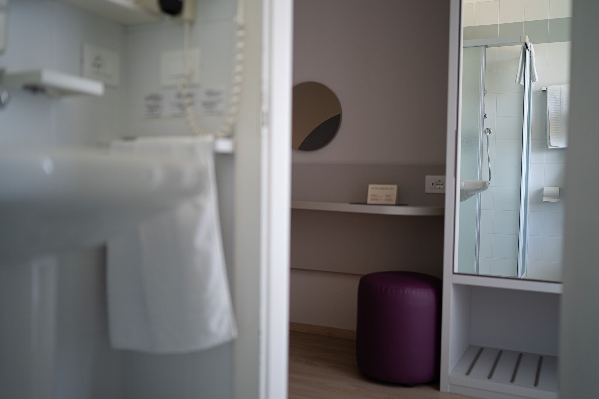 Un bagno moderno con cabina doccia in vetro, un lavandino bianco e uno sgabello viola.
