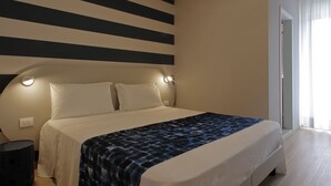 A modern bedroom with a large bed, a round ceiling light, and a striped wall design. - Hotel Smeraldo (Lignano Sabbiadoro)