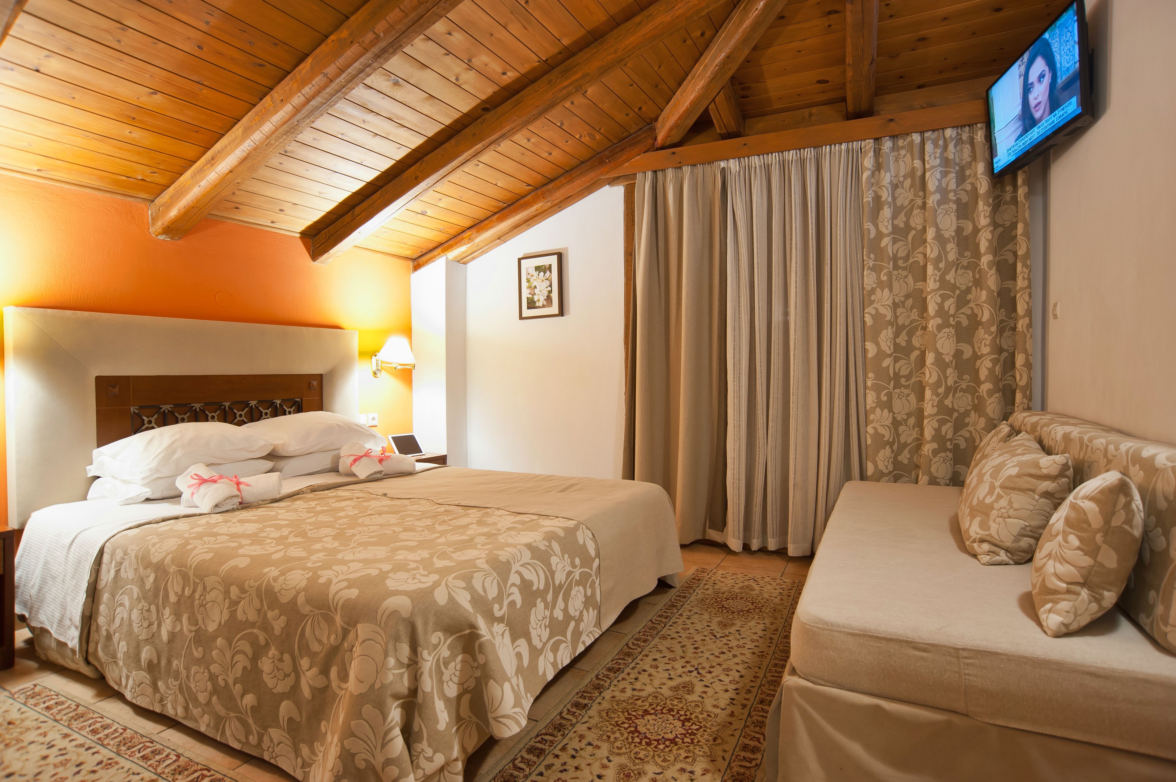 A hotel room with a bed, a sofa, a television, and a framed picture on the wall.