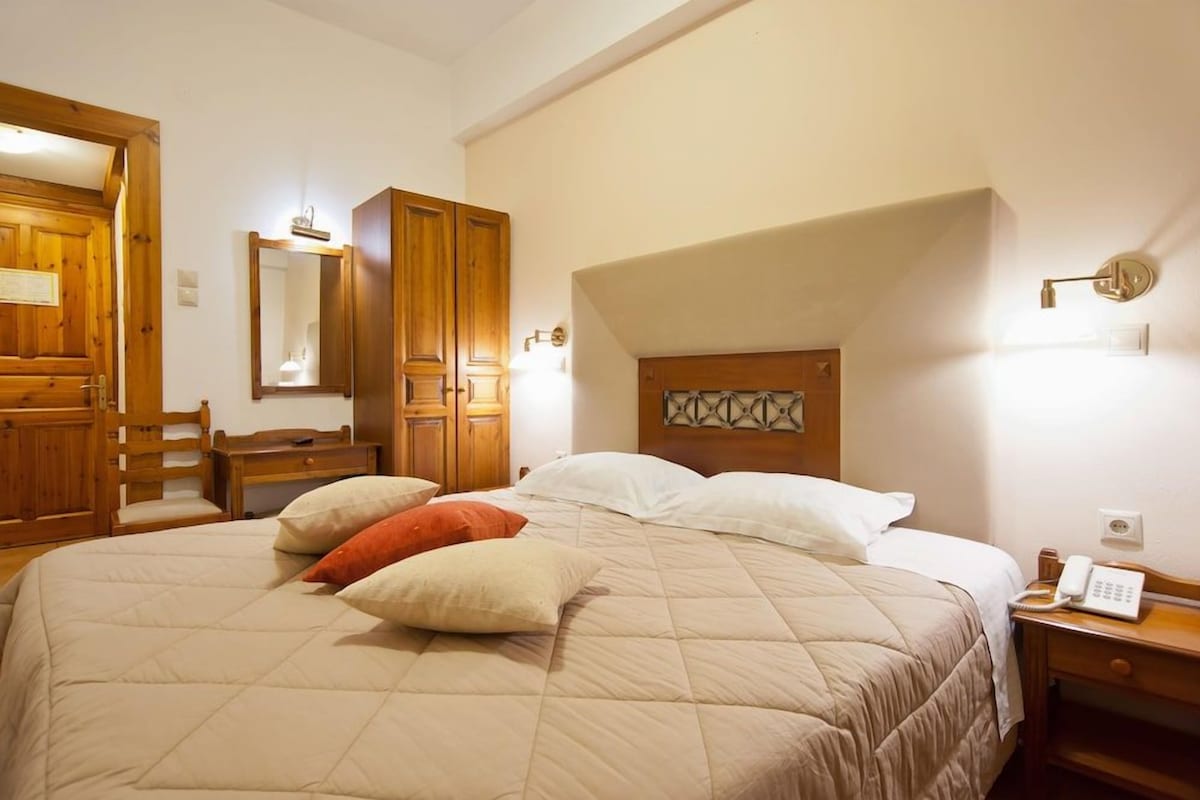 A hotel room with a large bed, wooden furniture, a desk, and a telephone.