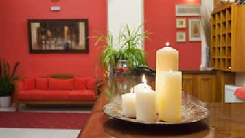 A room with a red wall, a wooden table with a plate of candles, a red sofa, and a plant.