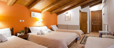 A hotel room with two beds, wooden beams on the ceiling, a small bedside table with a lamp, and a door leading to another room.