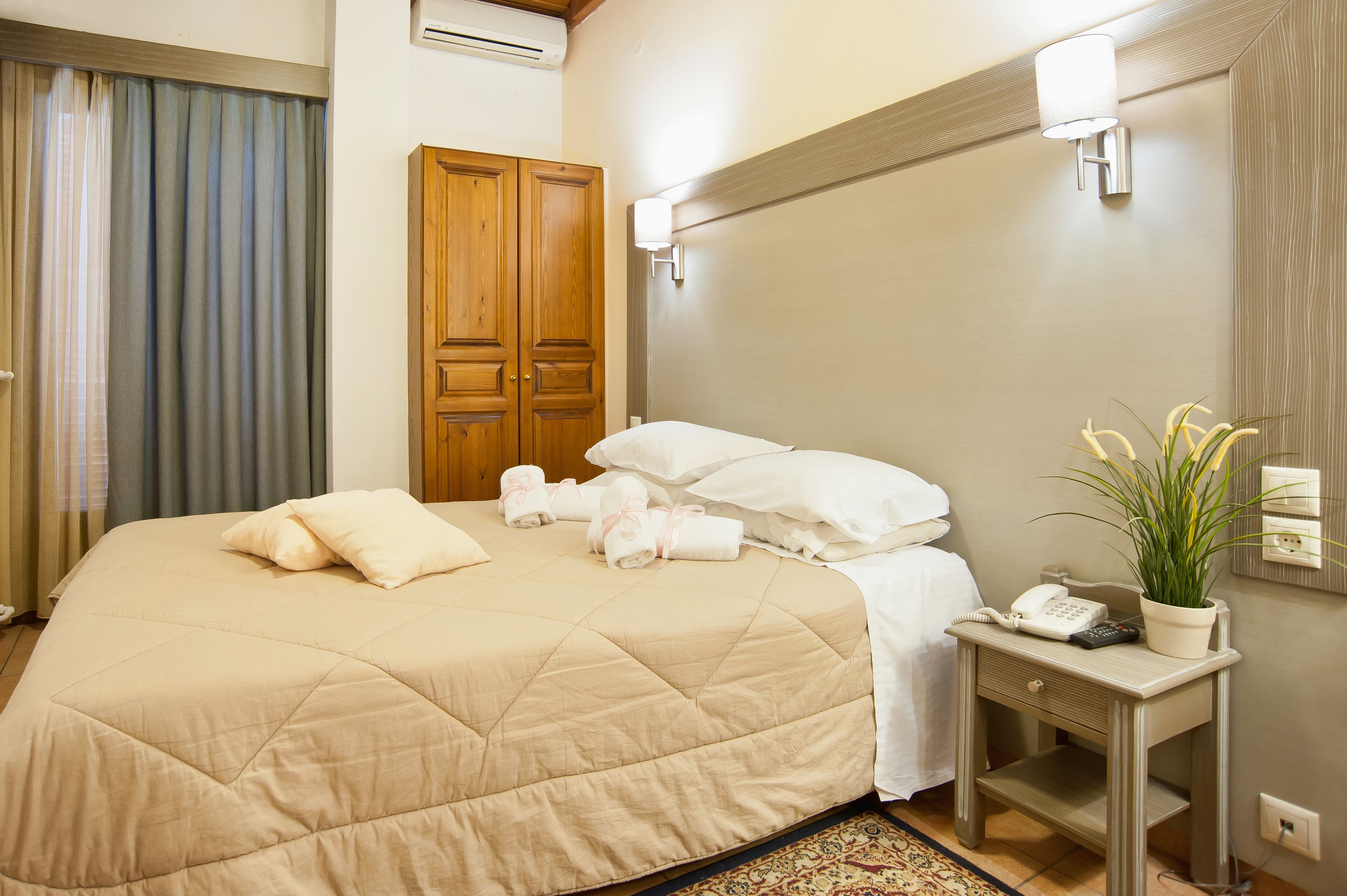 A hotel room with a large bed, a bedside table with a phone and a plant, and a wooden wardrobe.