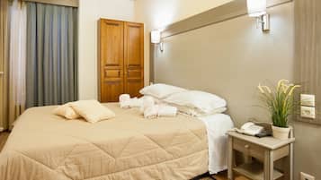 A hotel room with a large bed, a bedside table with a phone and a plant, and a wooden wardrobe.