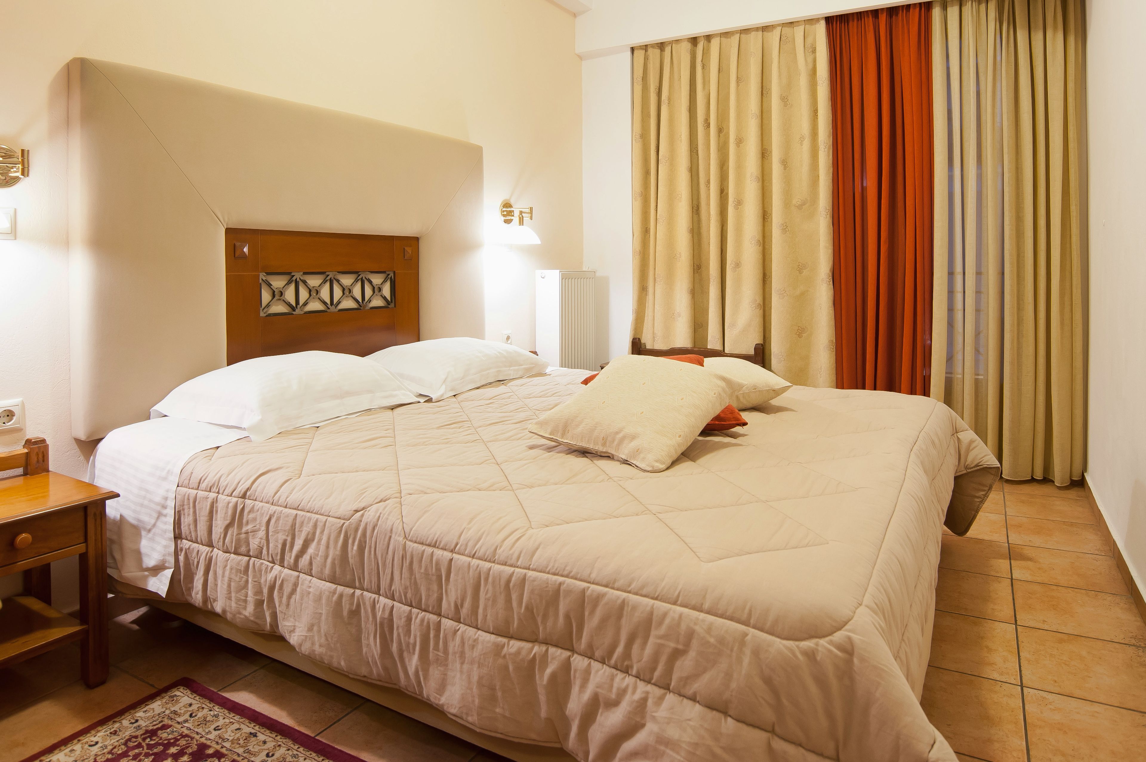 Une chambre d’hôtel avec un grand lit, une tête de lit en bois, une table de chevet et un radiateur.