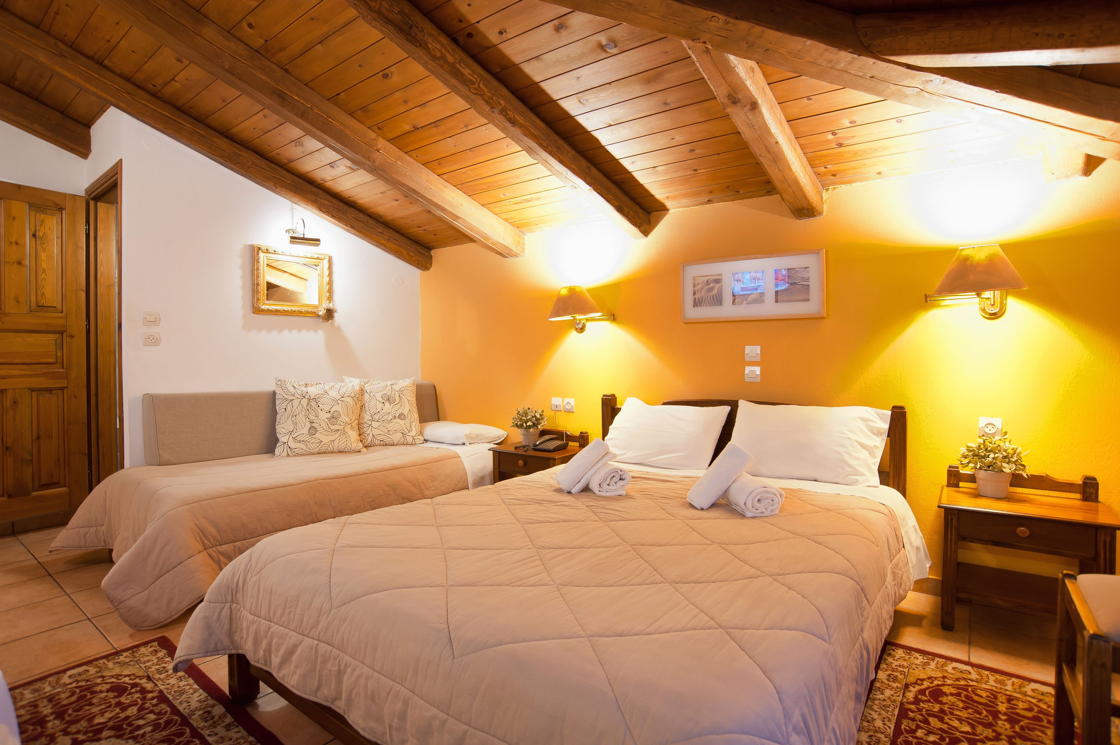Habitación de hotel con dos camas, vigas de madera en el techo y lámparas fijadas a la pared.