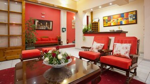 A living room with red sofas, a glass coffee table with a floral centerpiece, and a painting on the wall. - Pan Hotel (Delphi)