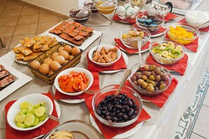 A buffet table with various food items including eggs, sausages, fruits, and olives.