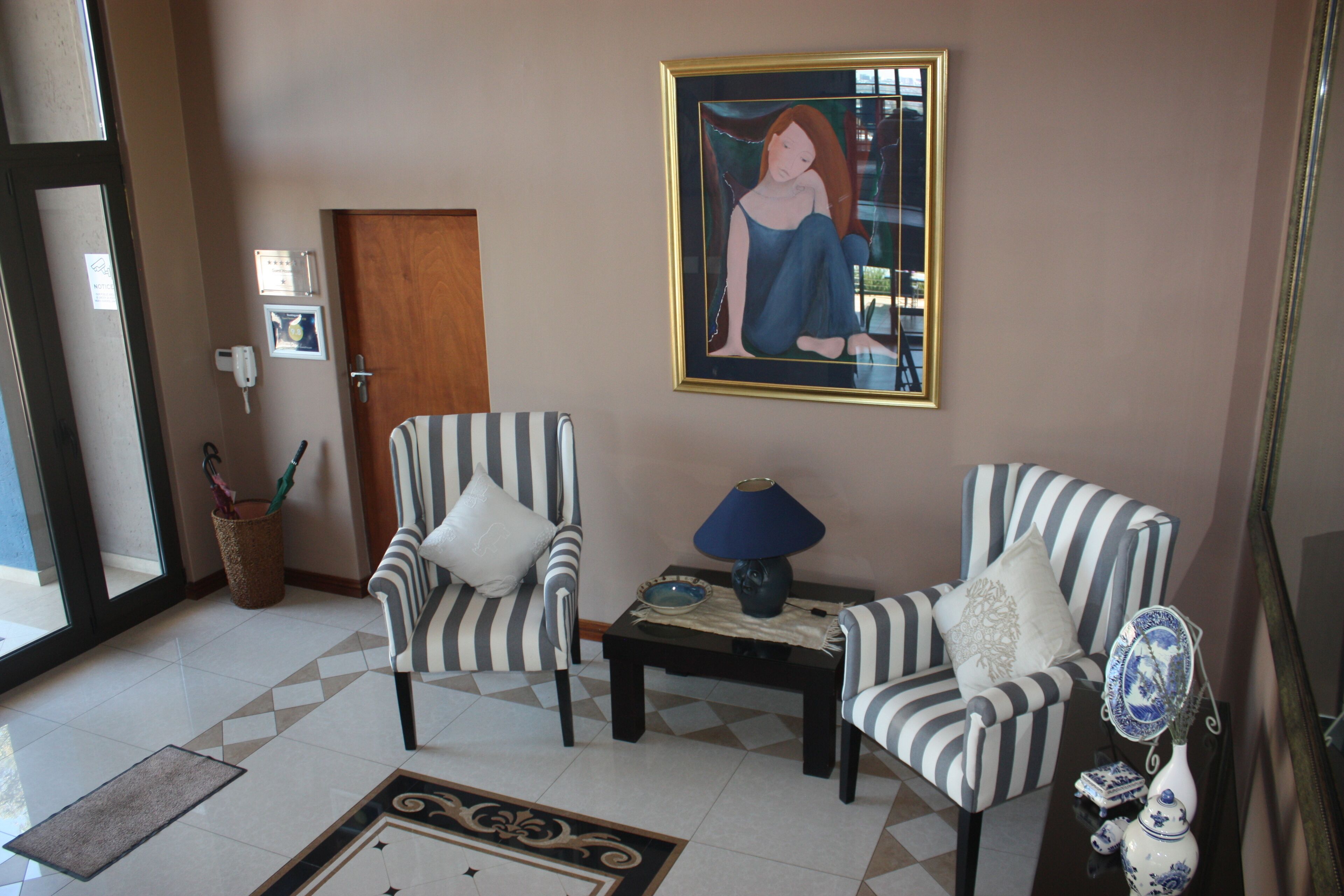 A living room with two striped armchairs, a small table with a lamp, a framed painting on the wall, and a vase with a mirror.