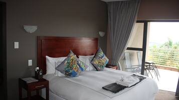 A hotel room with a large bed, two pillows, a bedside table with a lamp, and a view of the outdoors through a large window.