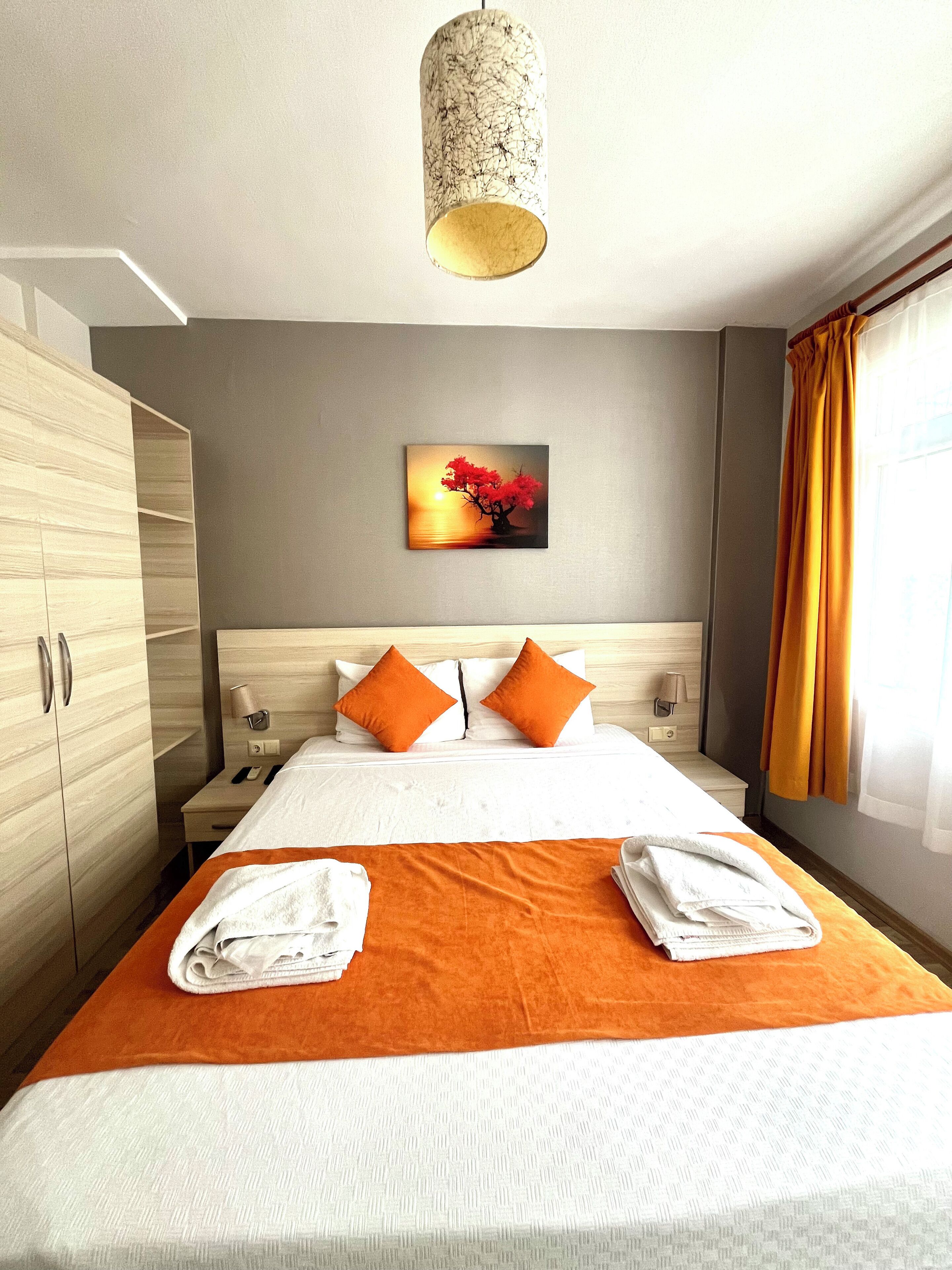 A hotel room with a bed, a nightstand, a lamp, a painting, and a wardrobe.