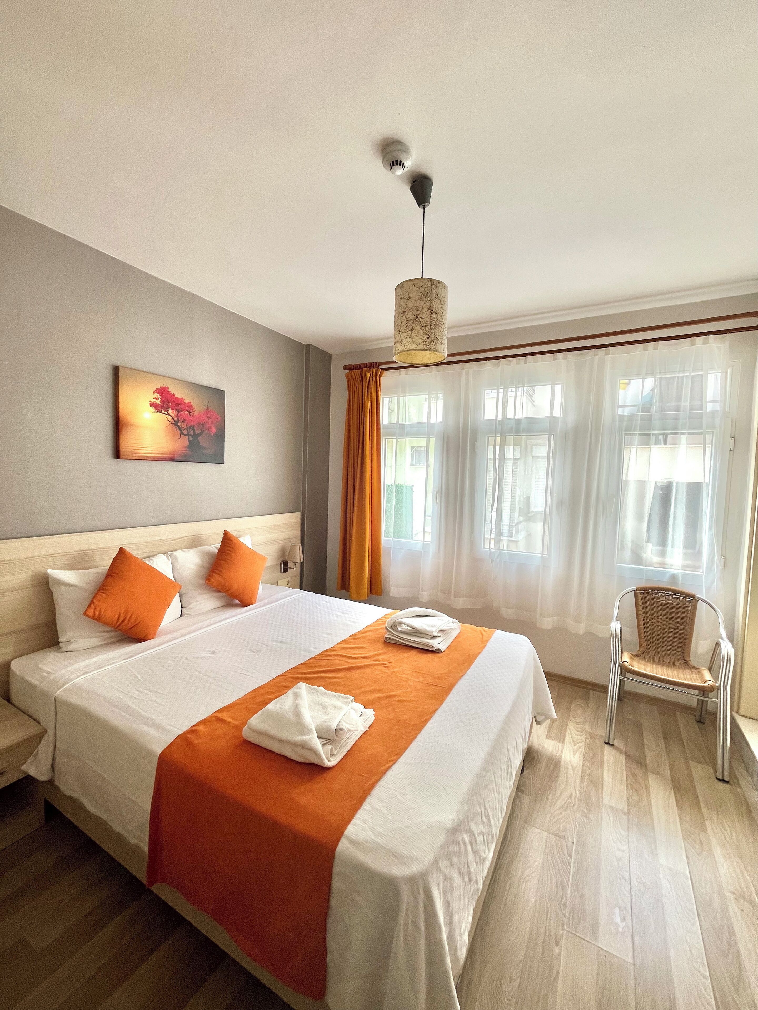 Hotellihuone, jossa on suuri sänky, seinällä taulu, tuoli ja ikkuna, jossa on verhot.